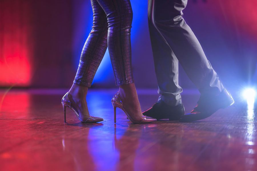 Nogi tańczącej pary, szpilki na parkiecie w kolorowym świetle