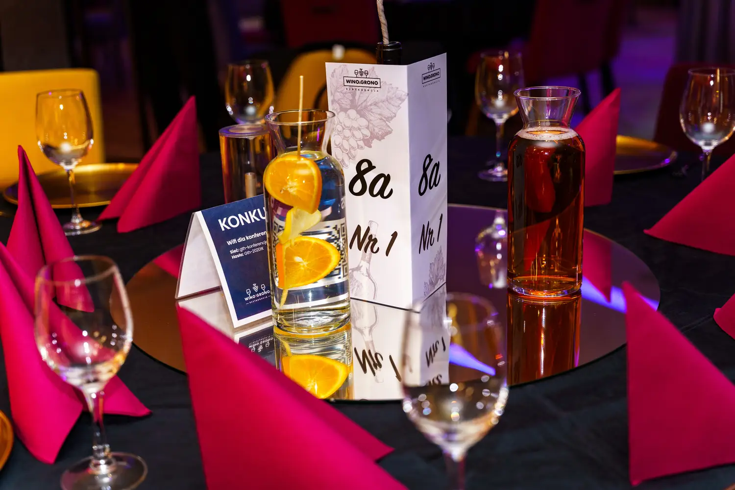 Szczegół nakrytego stołu: numer stolika, drink z pomarańczą i serwetki