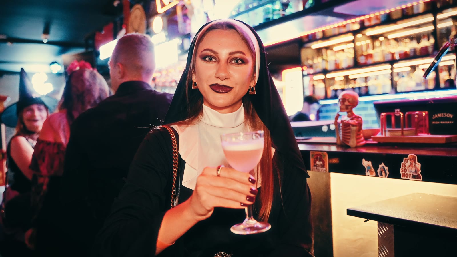 Gościni w przebraniu zakonnicy z koktajlem przy barze, za nią czarownica, Halloween 2025