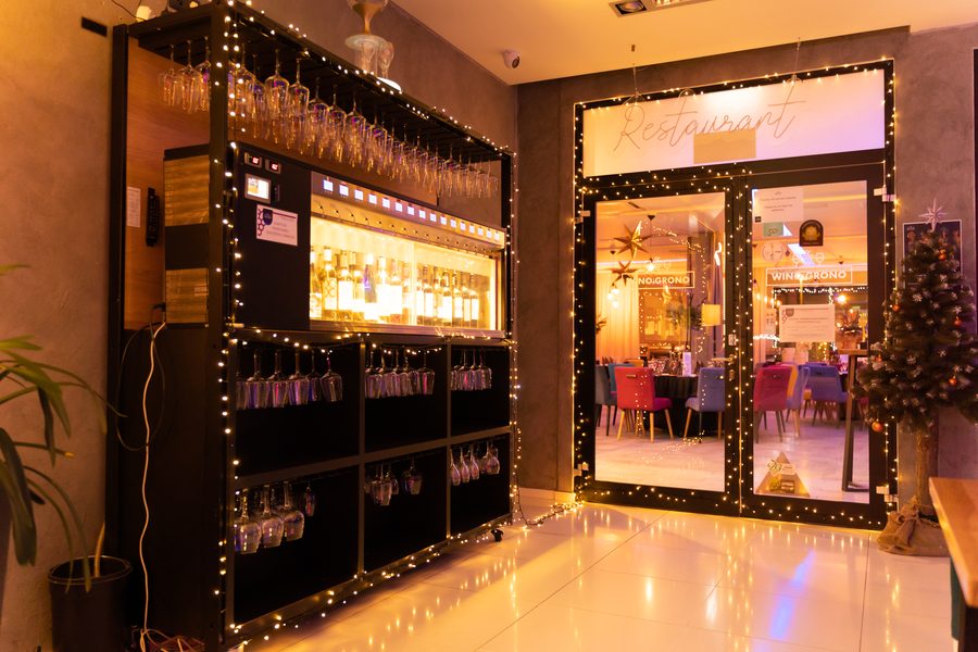 Wejście do restauracji udekorowane lampkami, regał z kieliszkami