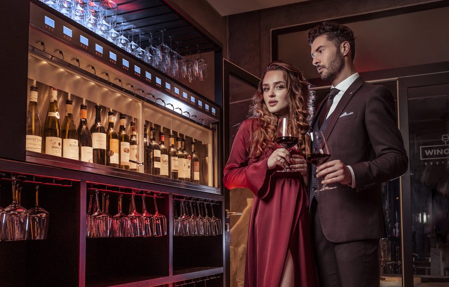 Elegancka para z winem przy podświetlonym regale z butelkami