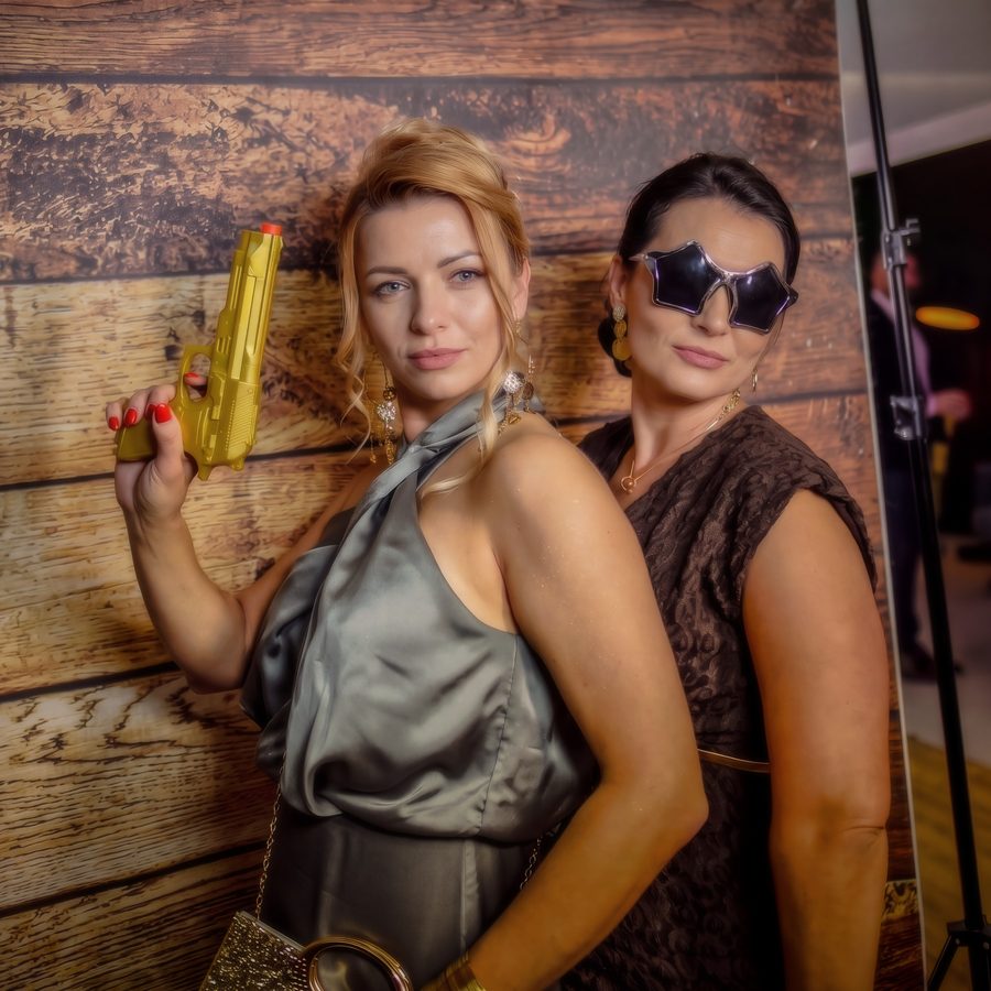 Dwie kobiety w wieczorowych strojach pozują w fotobudce