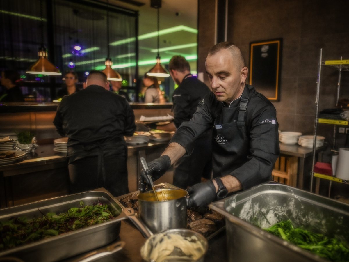 Kucharze w czarnych kitlach wydają dania w kuchni Wino i Grono