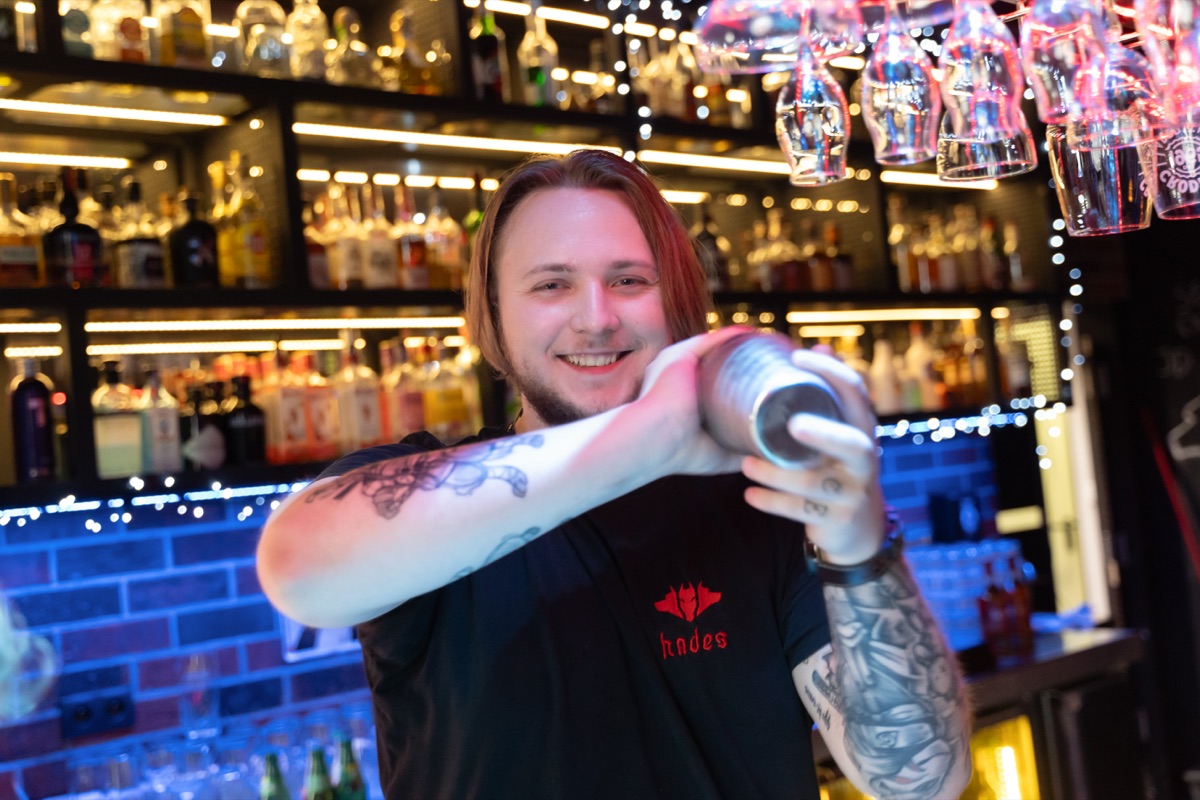 Uśmiechnięty barman Hadesu przygotowuje drinka w shakerze